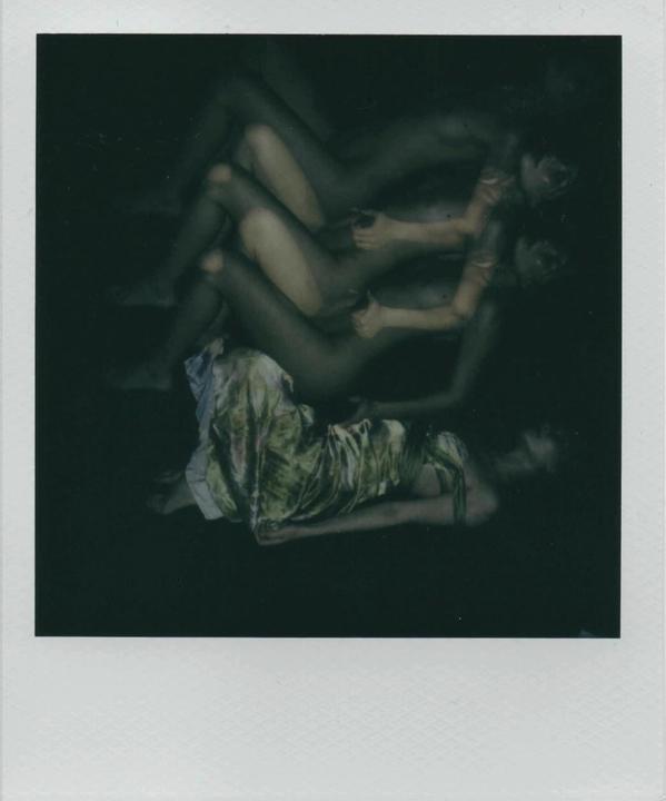 A woman in a green dress lies on a dark surface with multiple exposures of a nude woman superimposed above her.
