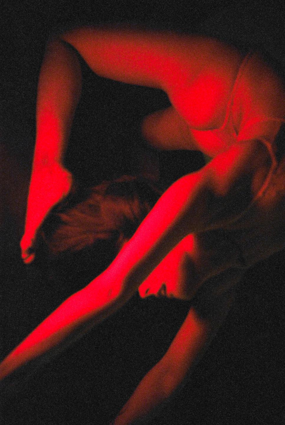 A woman is bathed in red light, with her body contorted and her head resting on a dark surface.