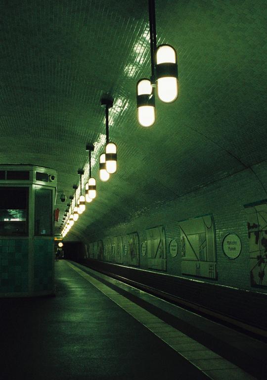 A subway platform with a tiled, arched ceiling is illuminated by a row of capsule-shaped lights.