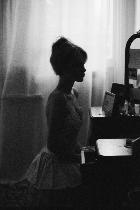 A woman in a short skirt and bra kneels in front of a vanity table, silhouetted against a window.