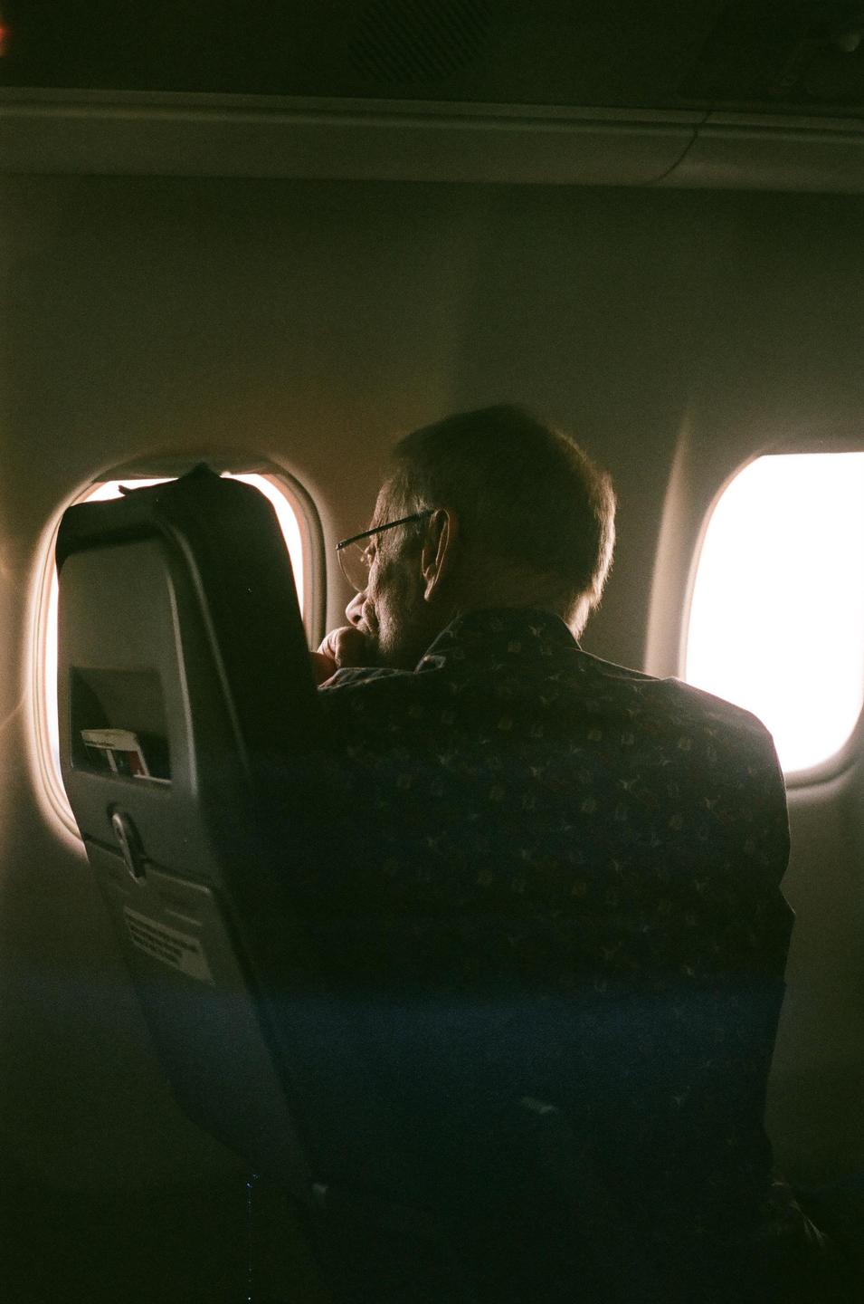 A man wearing glasses looks out of an airplane window.