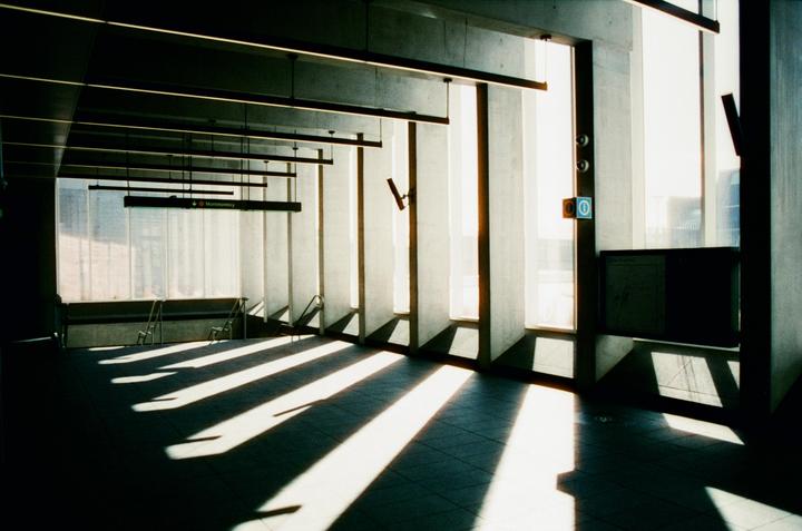 Sunlight streams through tall windows, casting long, diagonal shadows across the tiled floor of a large, empty room with a sign for Montmorency.