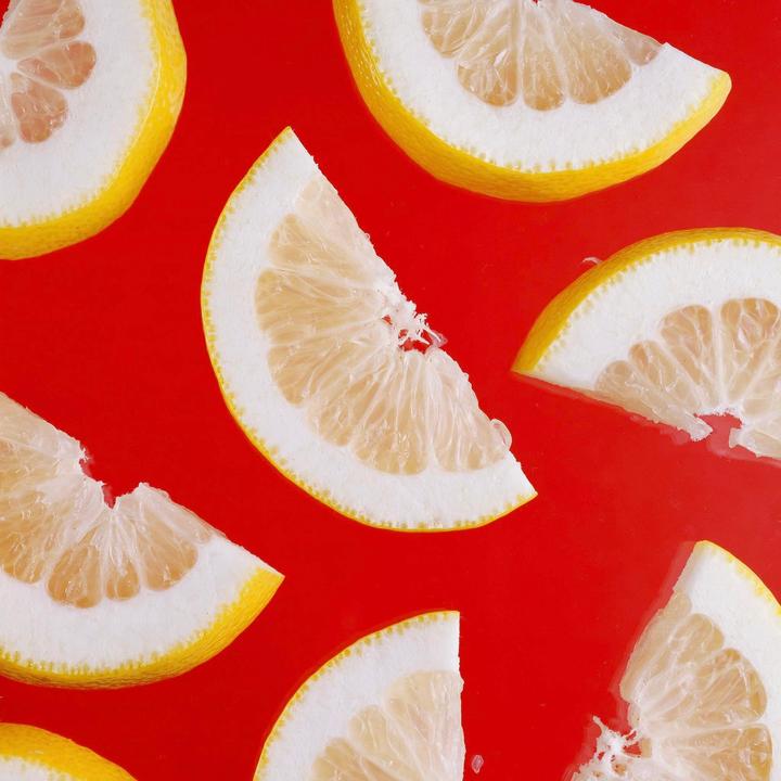 Several slices of lemon are arranged on a bright red surface.