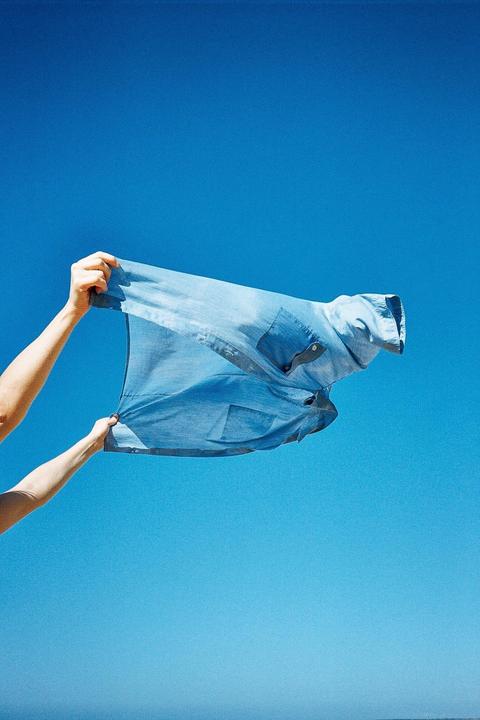 Two arms hold a blue shirt against a clear blue sky.