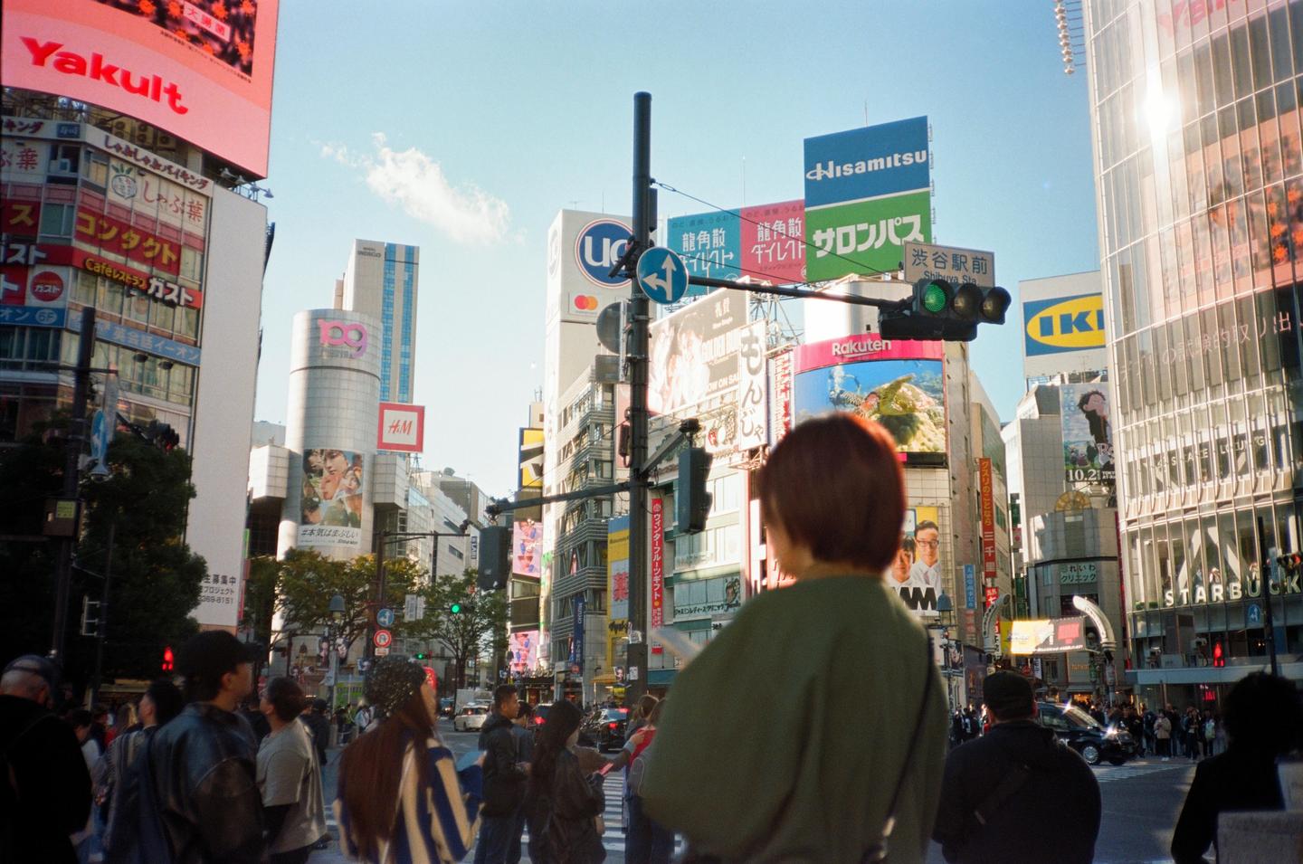 A woman stands in a busy Tokyo intersection surrounded by tall buildings and large advertisements.