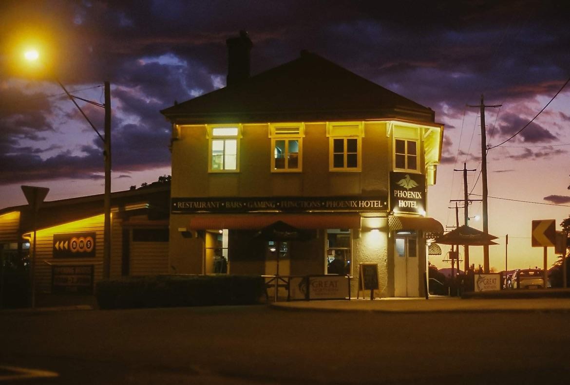 A hotel with illuminated windows and signs stands under a dramatic purple and orange sky at dusk.