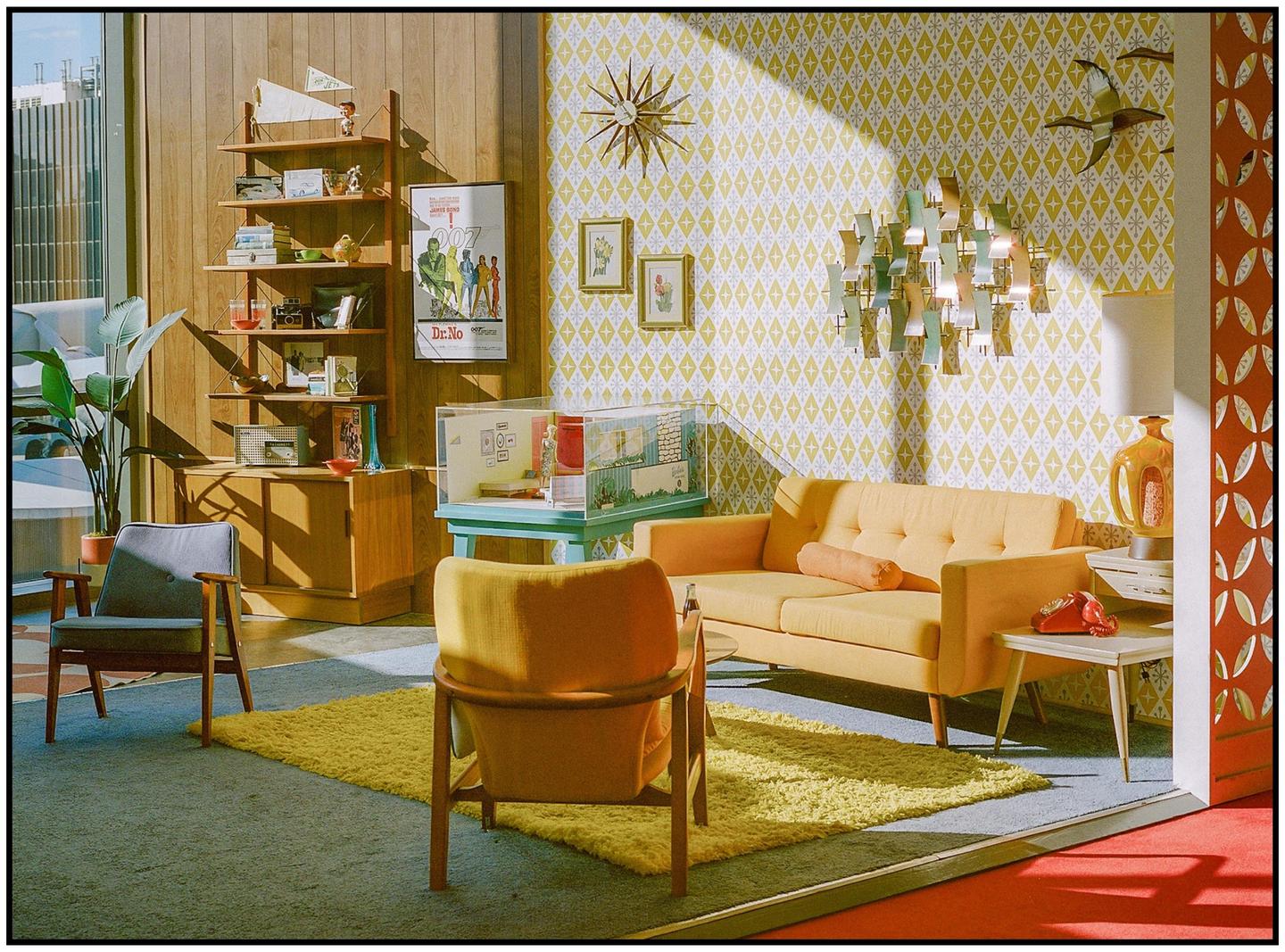 A mid-century modern living room is decorated with yellow and orange furniture and patterned wallpaper.