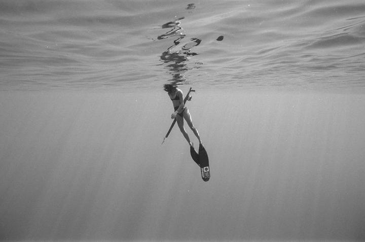A woman in a bikini and fins holds a speargun underwater.