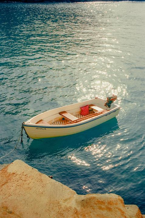A small boat named Anna floats on sparkling blue water next to a concrete dock.