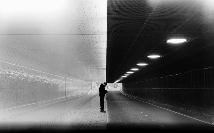 A man stands in a tunnel where one side is brightly lit and the other is dark with illuminated lights.