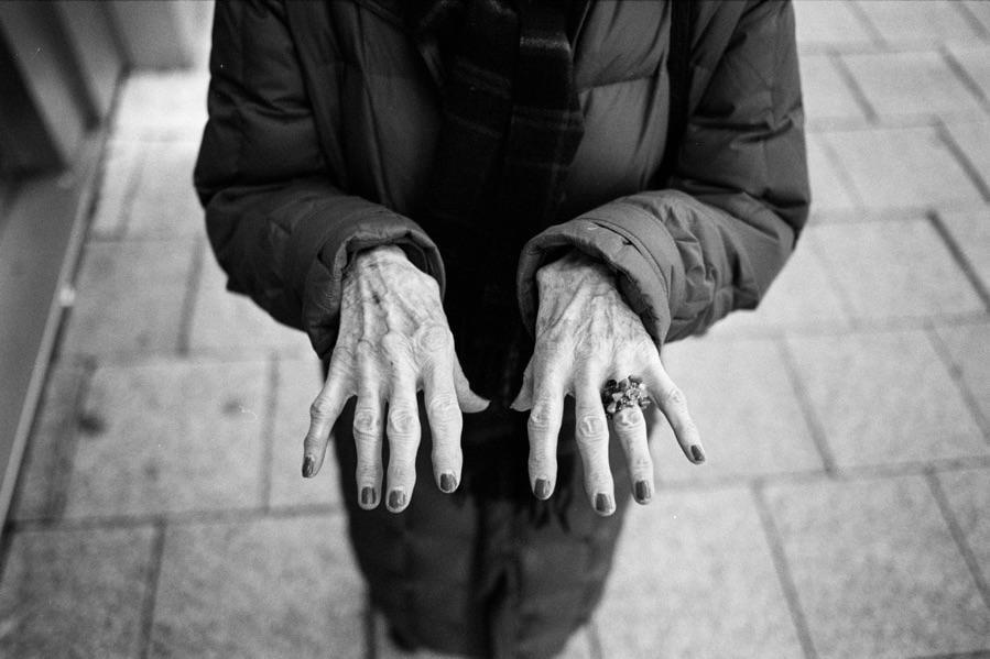 A person's wrinkled hands with painted fingernails and a ring are held out in front of them.