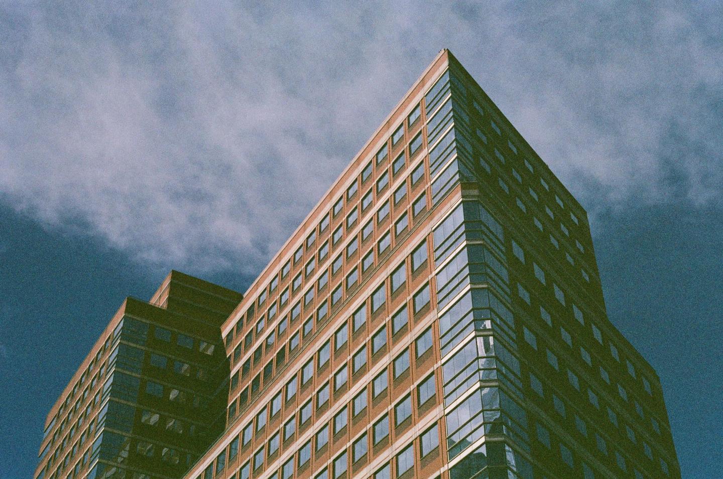 A tall building with many windows is seen from a low angle against a cloudy sky.