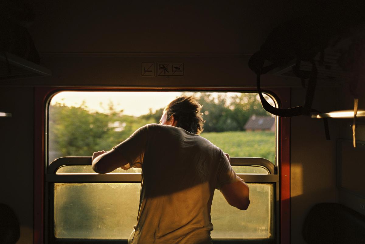 A man leans out of a train window, looking at the passing landscape.