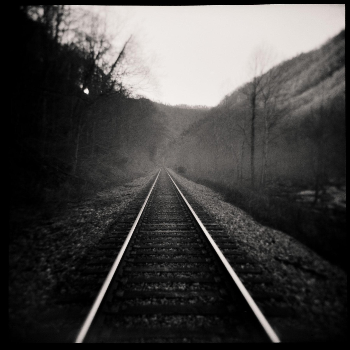 A set of railroad tracks extends into the distance through a valley with trees on either side.