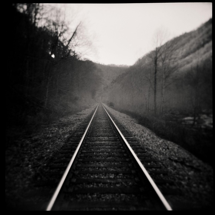 A set of railroad tracks extends into the distance through a valley with trees on either side.