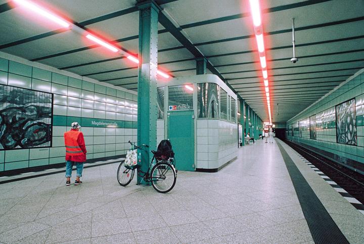 A person in a red jacket stands on a subway platform next to a bicycle.