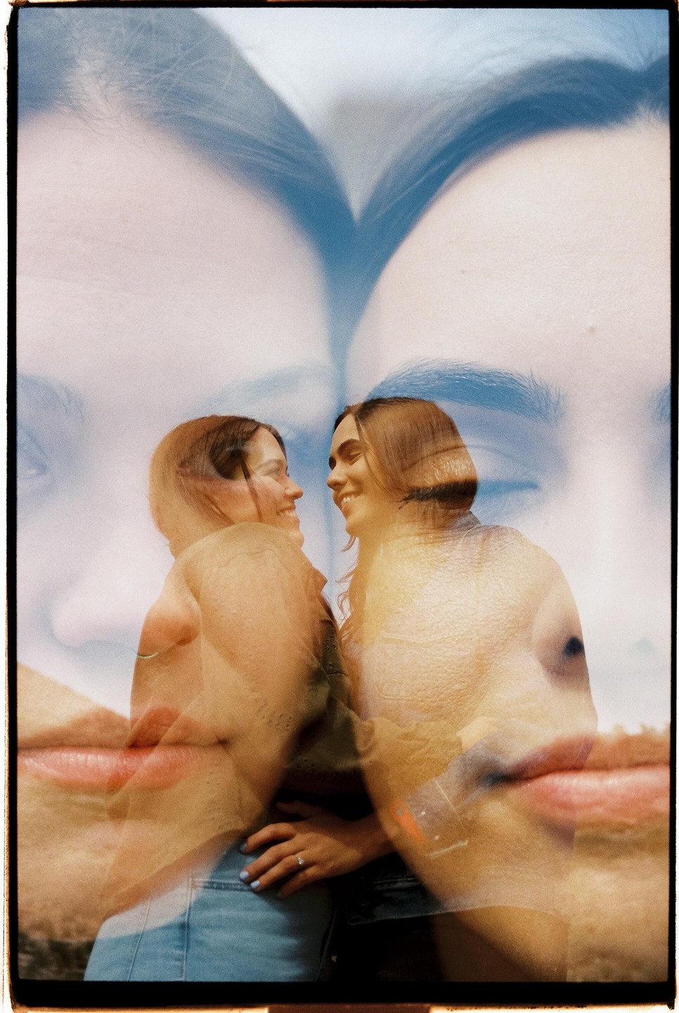 Two women smile at each other in a double exposure with two large faces in the background.