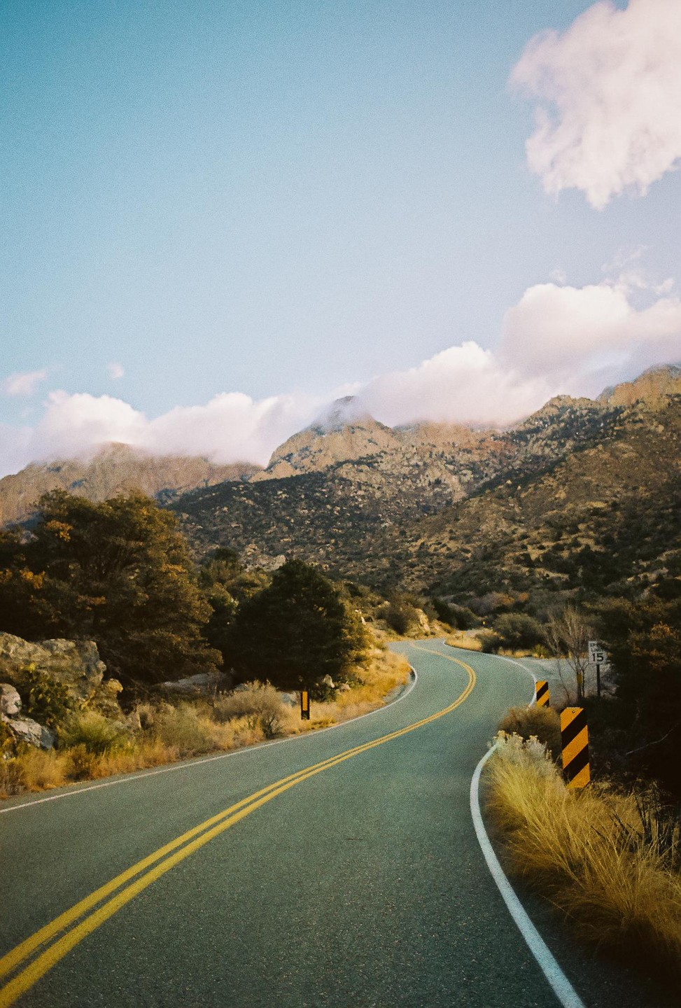 A winding road leads through a mountainous landscape with clouds partially obscuring the peaks.