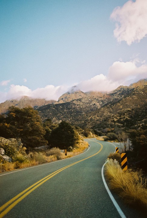 A winding road leads through a mountainous landscape with clouds partially obscuring the peaks.