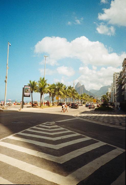 A street in Rio de Janeiro with mountains, palm trees, and a beach in the background.