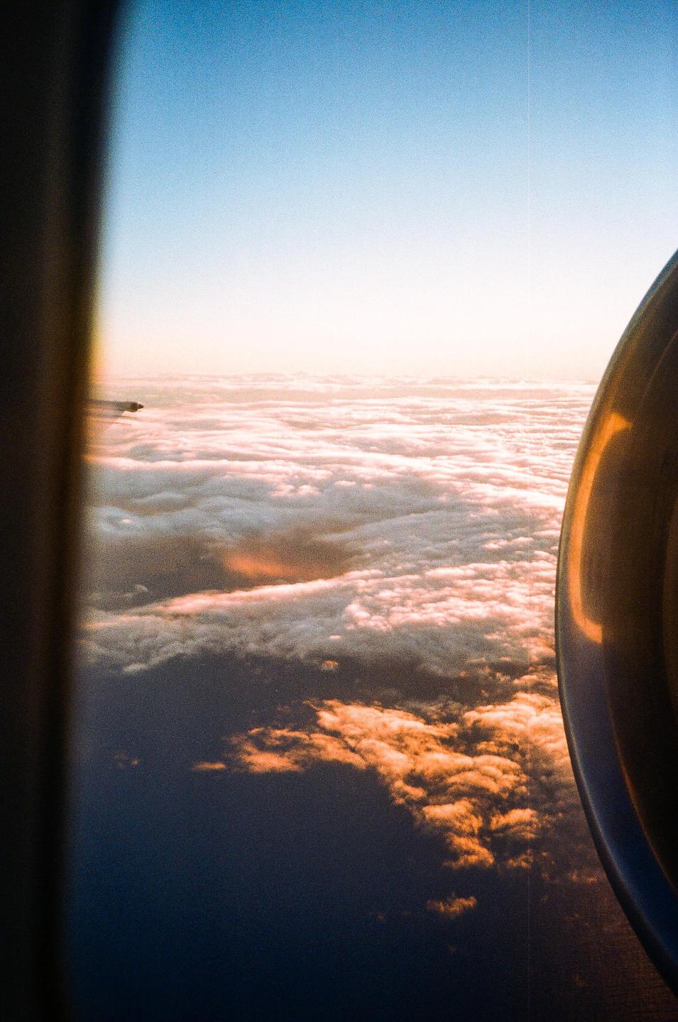 An airplane window view shows clouds and the ocean below during golden hour.