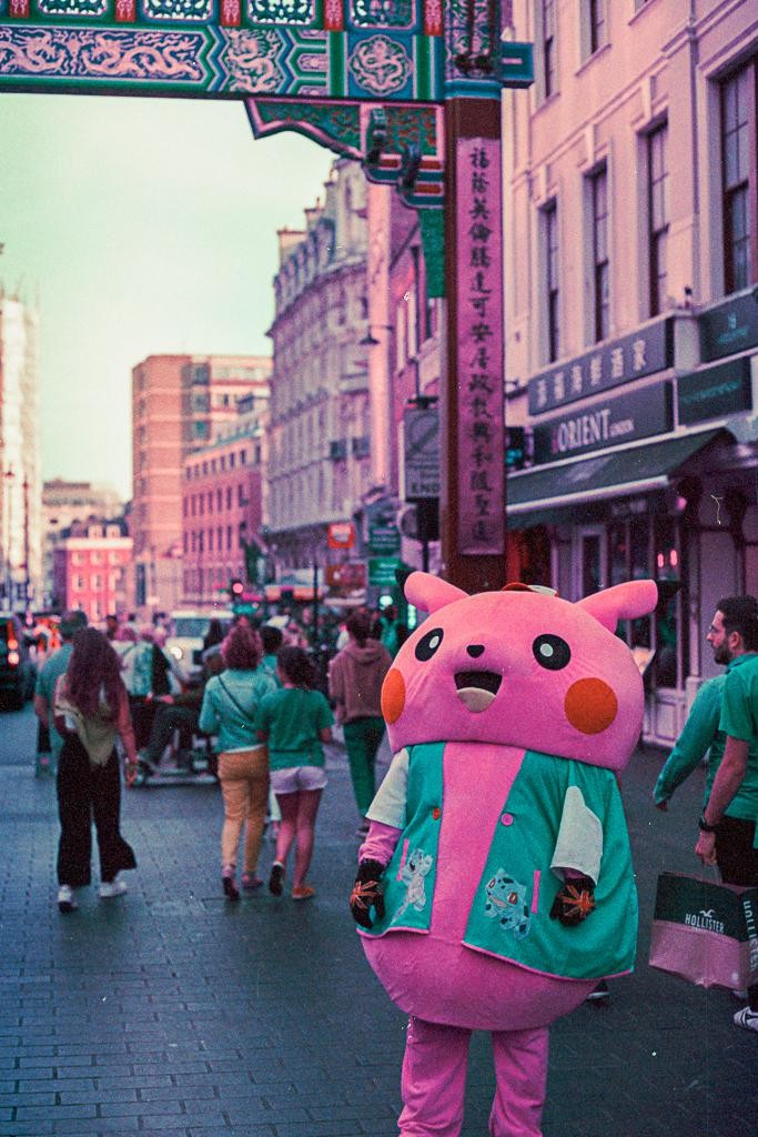 A person in a pink Pikachu costume stands on a street in Chinatown, London.