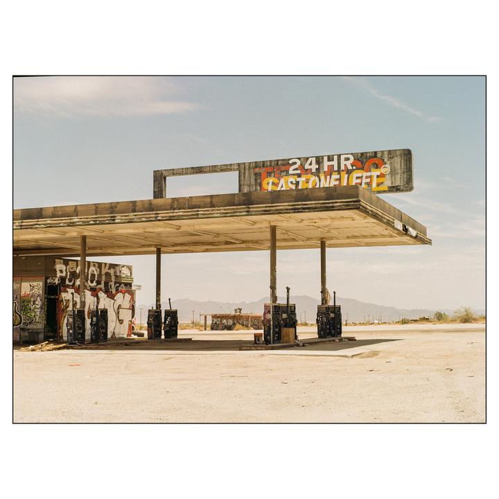 An abandoned gas station with graffiti on its walls stands in a desert landscape under a clear sky.
