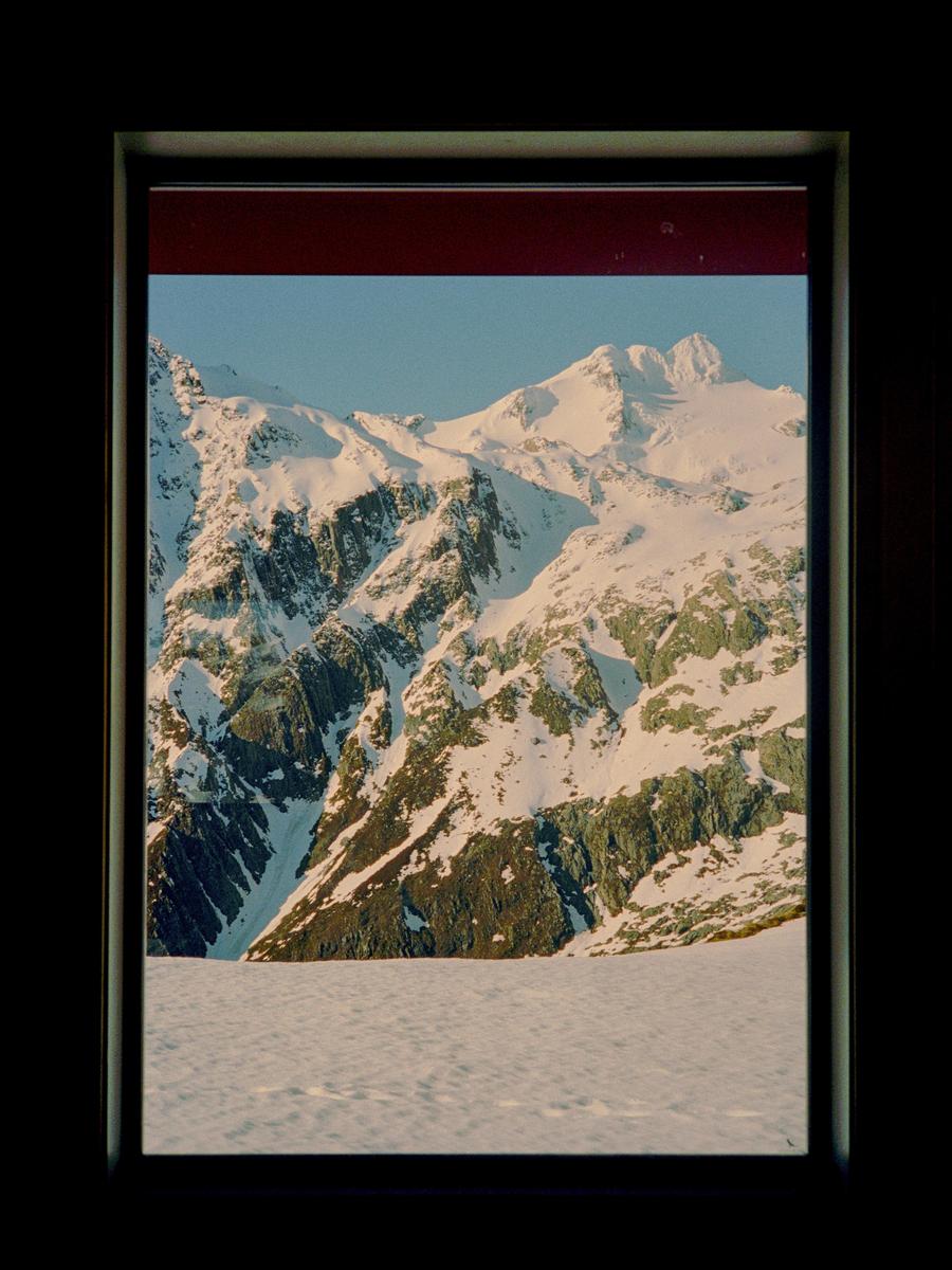 A snow-covered mountain range is visible through a window frame.