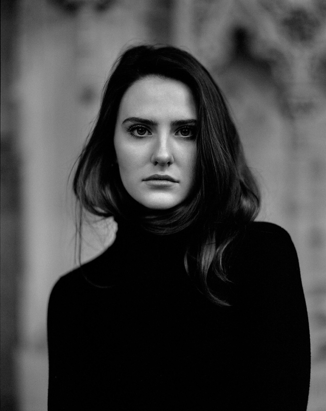 A woman with long hair and a dark turtleneck sweater looks directly at the viewer.