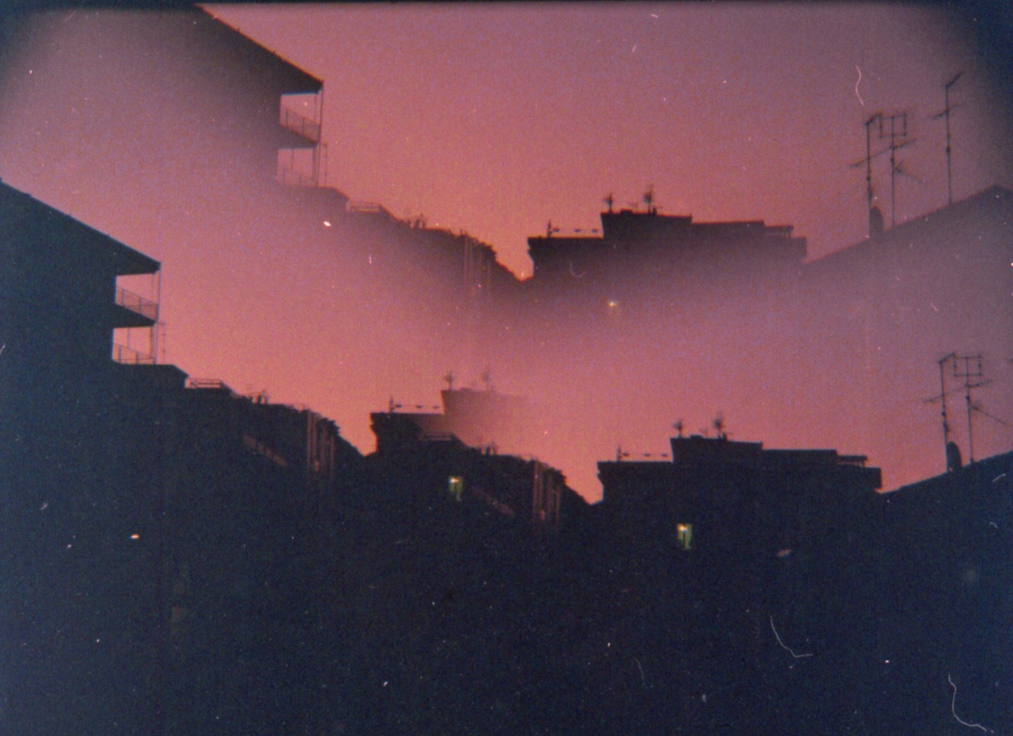 A hazy, dark cityscape is silhouetted against a vibrant pink and orange sky.