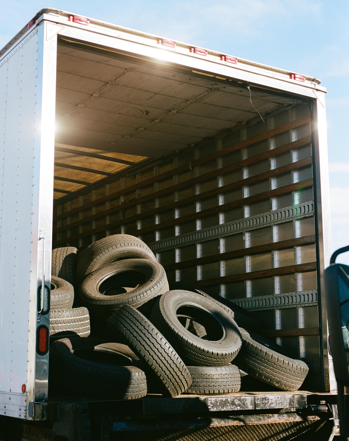 A truck bed is filled with a large pile of tires under a bright sky.
