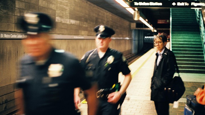 Two police officers and a man are on a subway platform at Pershing Square station.