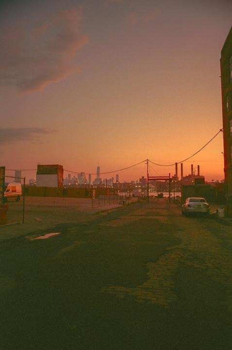 A city skyline is visible in the distance over an industrial area at sunset.