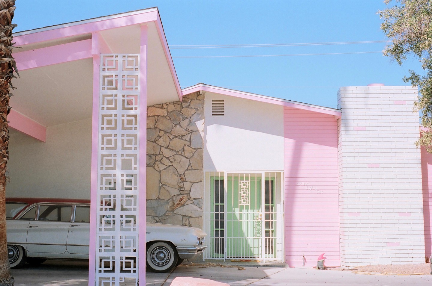 A pink and white house with a green door and a white car parked in the carport is visible under a clear blue sky.