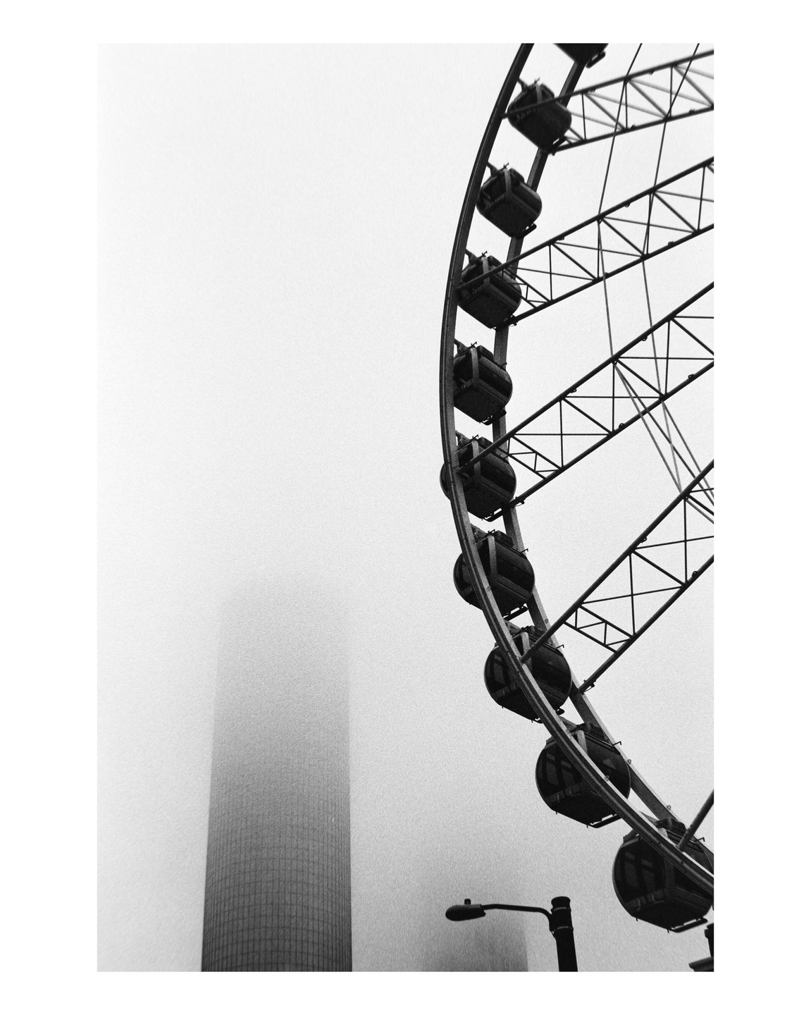 A ferris wheel is partially visible next to a tall building shrouded in fog.