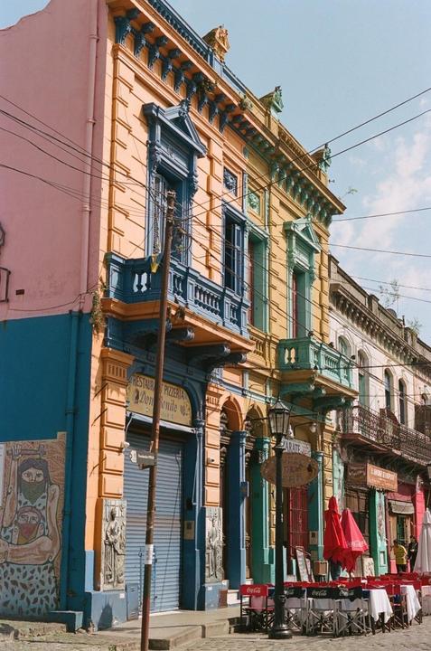 A street in Buenos Aires is lined with colorful buildings and a restaurant with red umbrellas.