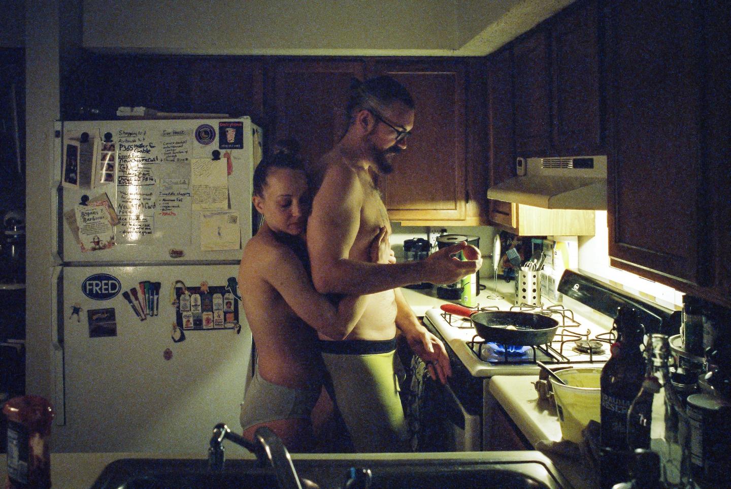 A couple embraces in a kitchen while cooking on a gas stove.