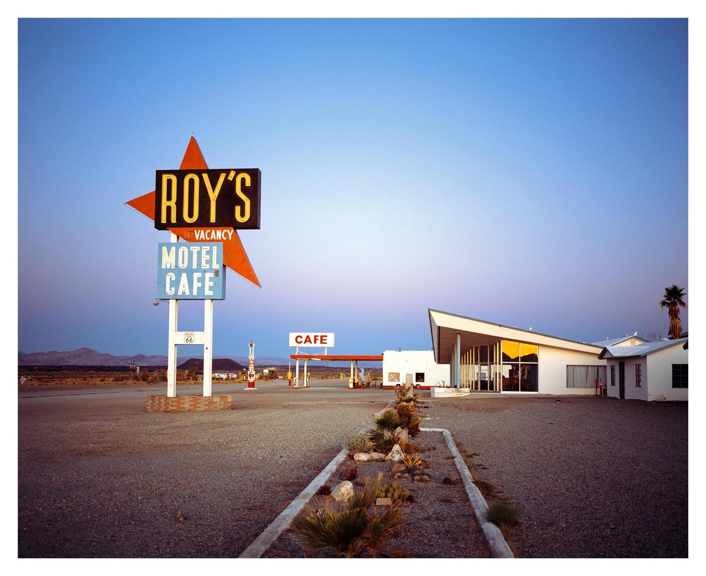 A motel and cafe sign stands in a desert landscape under a clear sky.