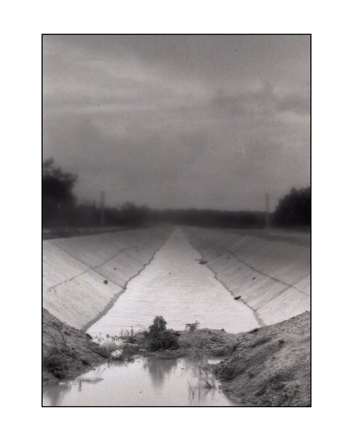A concrete irrigation canal stretches into the distance under a cloudy sky.