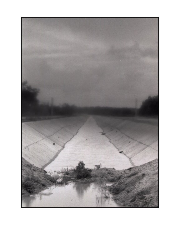 A concrete irrigation canal stretches into the distance under a cloudy sky.