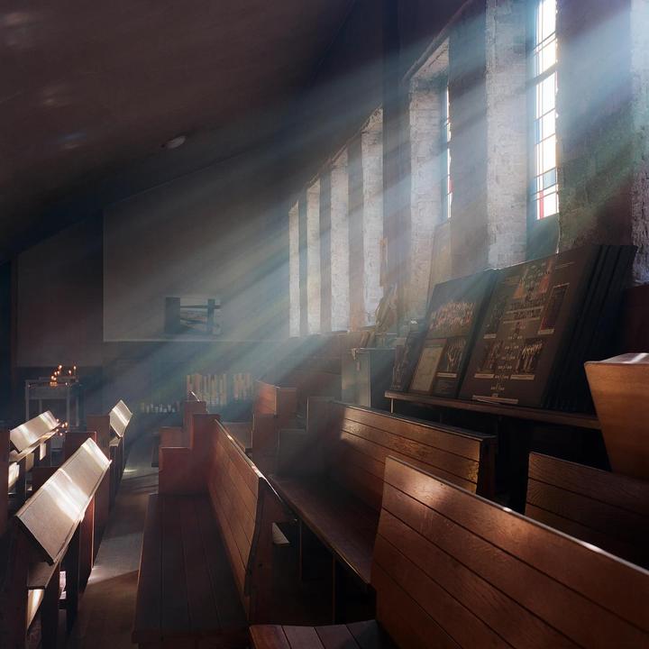 Sunlight streams through tall windows into a church interior with wooden pews.