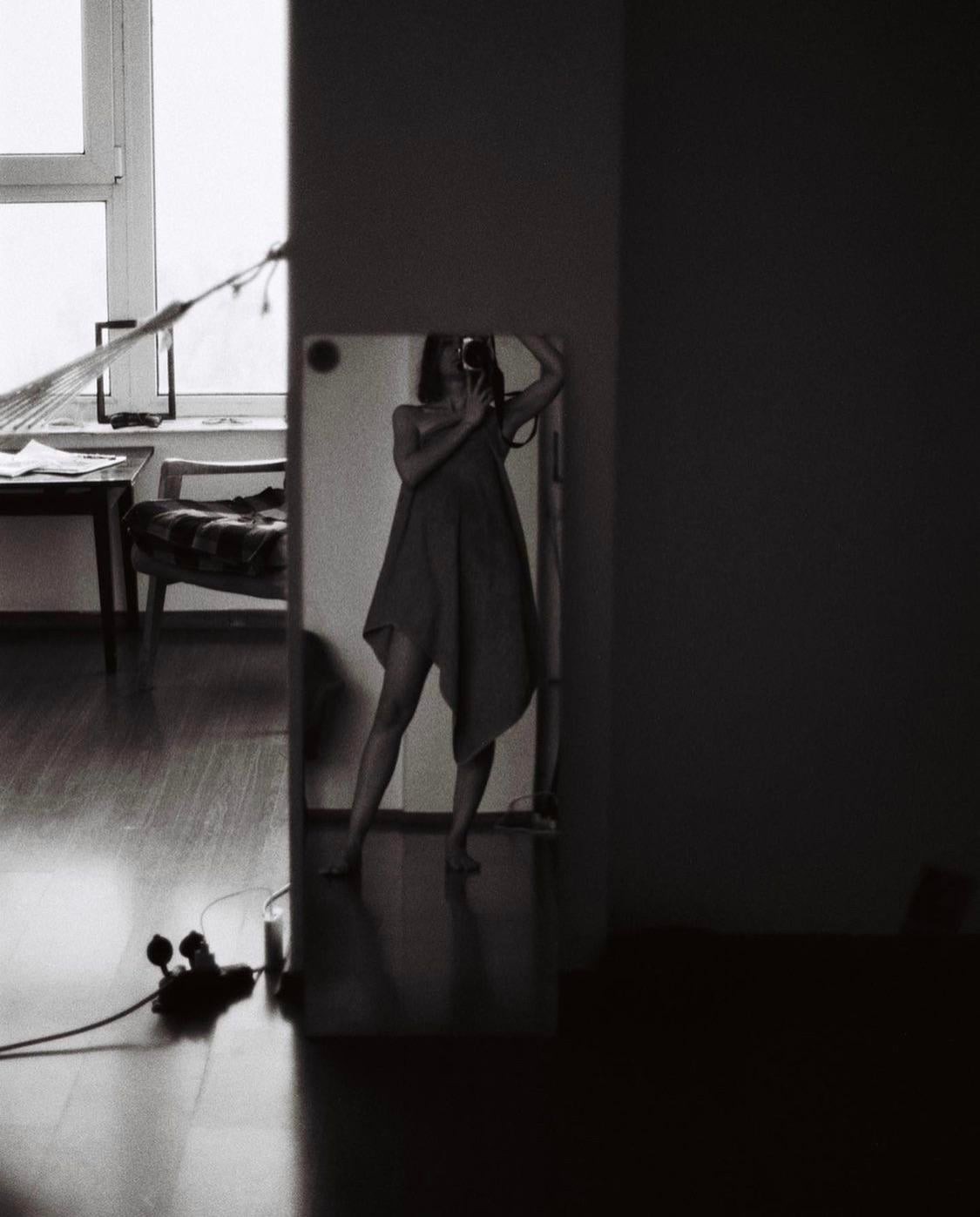 A woman takes a self-portrait in a mirror, holding a camera to her face.