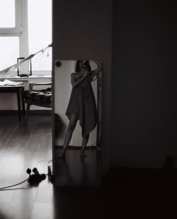 A woman takes a self-portrait in a mirror, holding a camera to her face.