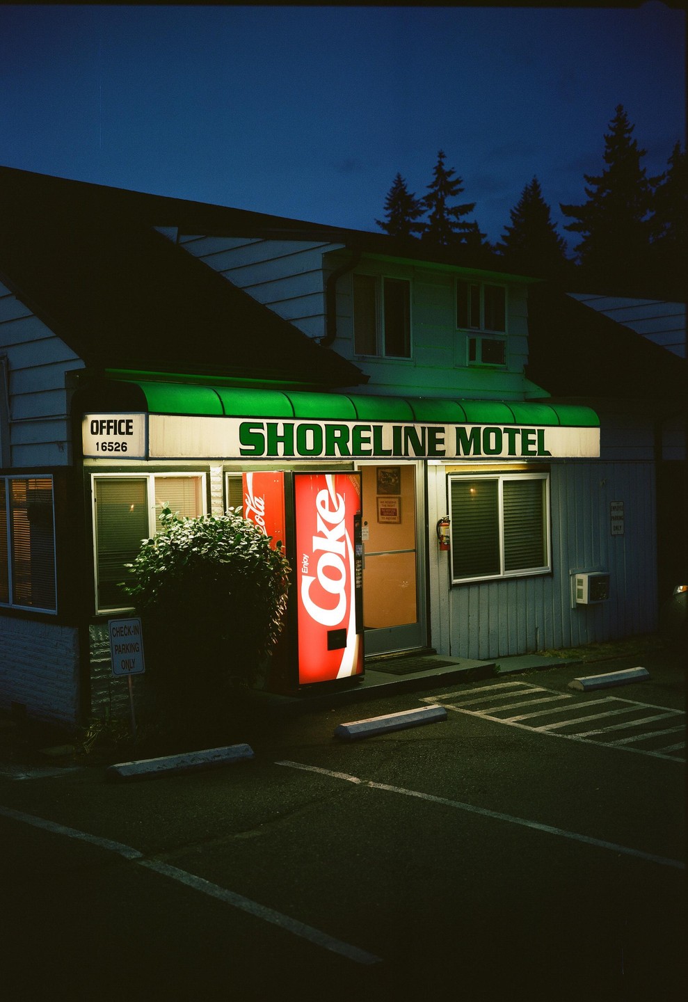 A red Coca-Cola vending machine stands outside the Shoreline Motel office at night.