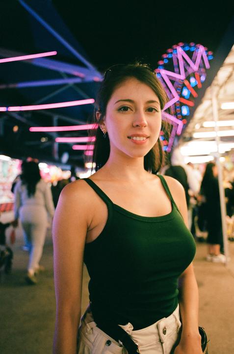 A woman in a green tank top smiles at the camera with neon lights in the background.