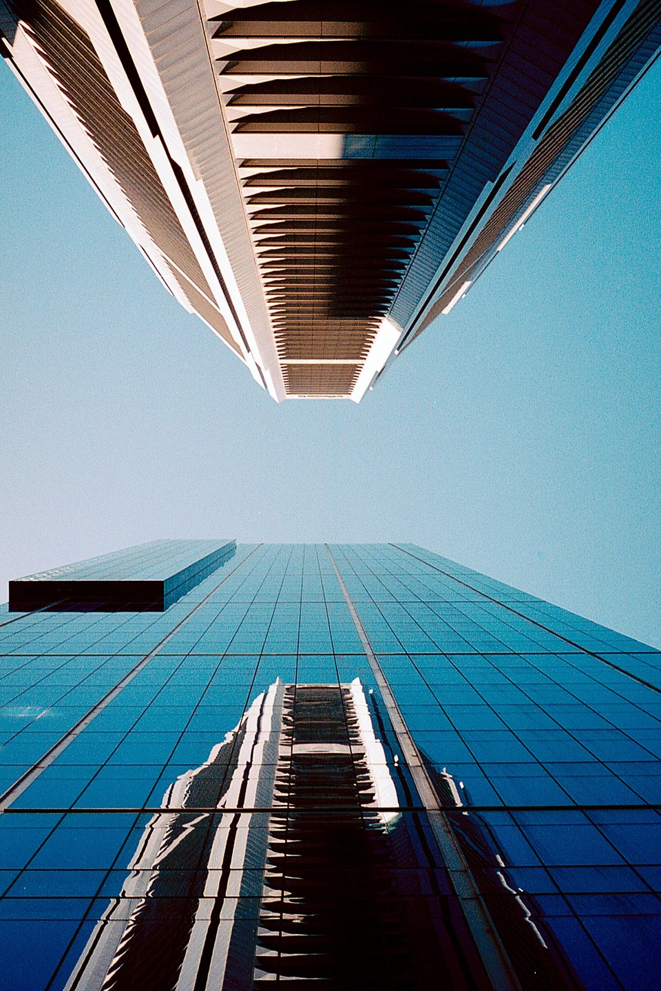 Two skyscrapers are visible from a low angle, with one reflecting the other.