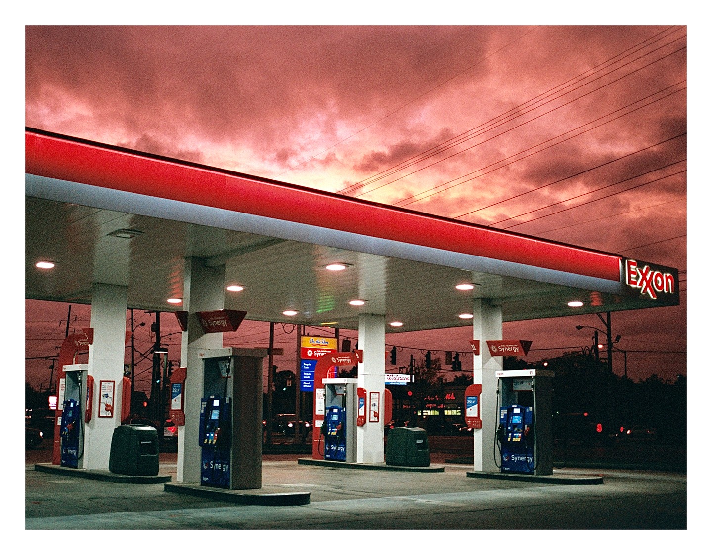A gas station with a red roof is illuminated under a dramatic red sky.
