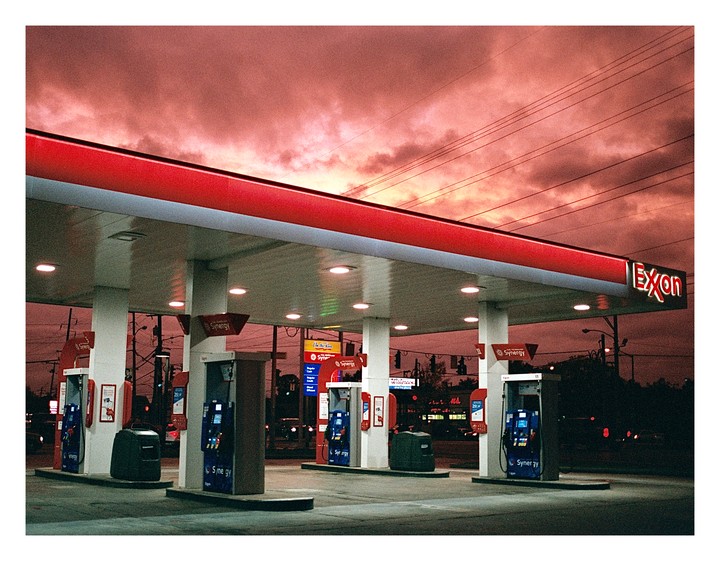 A gas station with a red roof is illuminated under a dramatic red sky.