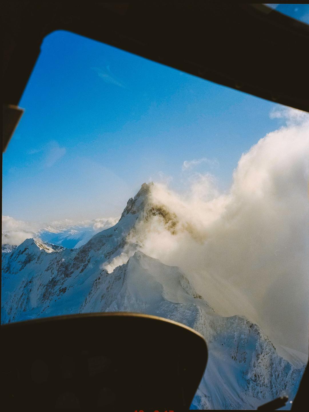 A view of snow-covered mountains and clouds from an aircraft window.