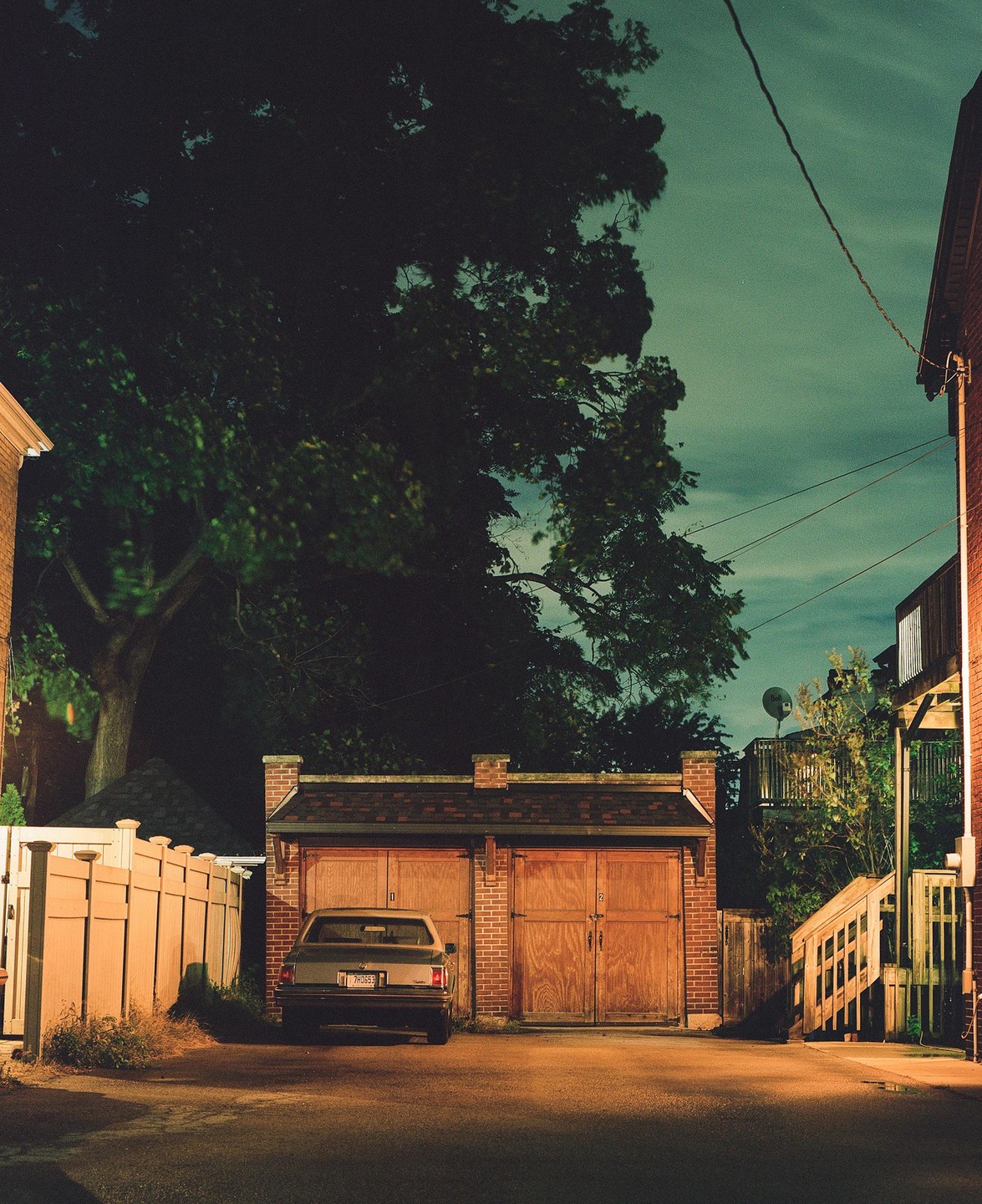 A car is parked in front of a brick garage with two wooden doors at night.
